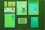 Green office supplies and digital touch screen tablet on the grass, business and ecology concept