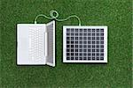 Laptop on the grass connected to a solar panel, alternative energy sources and electrical power generation concept