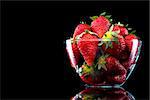 Delicious strawberries in a glass bowl on black background.