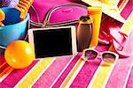 Empty touch screen tablet with colorful beach towel, sunglasses, sun creams and beach accessories.