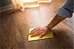 Male hand cleaning and rubbing an hardwood floor with a microfiber cloth.