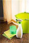 Spray detergent with green bucket, sponge and pads on living room hardwood floor.