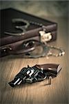 Vintage revolver and bullet with briefcase and handcuffs on background.