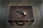 Vintage revolver gun on leather briefcase with bullet on wooden table.
