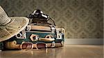 Vintage luggage with sunglasses, camera and straw hat on wooden floor.