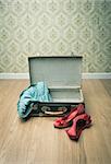 Open vintage suitcase with red shoes and dotted clothing, retro wallpaper on background.
