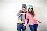 Two Happy Smiling Hipster Girls Posing at White Brick Wall Background. Trendy Casual Fashion Outfit in Autumn or Spring. Teenage Friendship and Lifestyle Concept. Toned Photo with Copy Space.