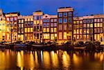 Typical dutch houses over canal with reflections illuminated at night, Amsterdam, Netherlands