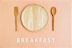 Top view of wooden dish fork spoon with breakfast wording on light orange background