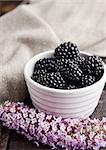 Blackberry in white bowl and flowers on wooden background. Natural healthy food.Still life photography