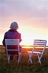 Woman sitting on wooden chair on meadow