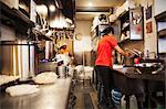 The ramen noodle shop. A chef working in a kitchen preparing food using a stove and large pans.