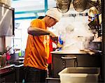 The ramen noodle shop. Staff preparing food in a steam filled kitchen.