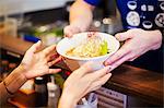 The ramen noodle shop. A chef offering a white bowl of ramen noodle broth to a customer