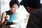 A ramen noodle cafe in a city.  A man and woman seated eating noodles from large white bowls.