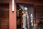 A small artisan producer of specialist treats, sweets called wagashi. A woman at the doorway of the shop.