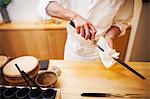 A chef working in a small commercial kitchen, an itamae or master chef preparing to make sushi, cleaning his knife.