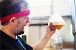 A brewer with a red bandana taking a jug of brewing beer and examining it.