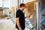 A brewer with a red bandana taking a jug of brewing beer and examining it.