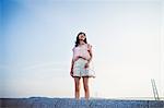 Young woman in shorts and pink shirt standing alone in open space, with a large suspension bridge in the background