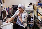 A mature woman at a desk in the office of a noodle production factory on the telephone.