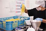 Workers in aprons and gloves weighing and packing freshly made noodles in a soba noodle production unit.