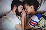 Couple looking at each other while lying on bed at bedroom