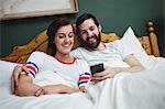 Couple using mobile phone on bed at bedroom