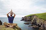 Man performing yoga on cliff