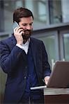 Businessman talking on mobile phone while using laptop