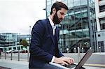 Attentive businessman using laptop outside office