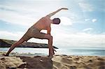 Rear view of man performing stretching exercise on beach