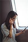 Young woman talking on mobile phone while using digital tablet