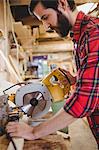 Man cutting wooden plank with electric saw in boatyard