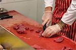 Mid section of butcher chopping red meat at butchers shop