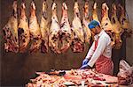 Butcher chopping meat in storage room at butchers shop