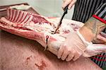 Mid section of butcher cutting the ribs of pork carcass in butchers shop