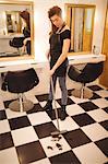 Female hairdresser cleaning hair waste on floor with broom at saloon