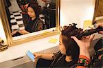 Woman using mobile phone while getting her hair straightened at hair saloon