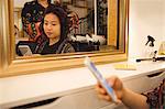 Woman using mobile phone while getting her hair straightened at hair saloon