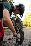 Male cyclist repairing his bicycle in forest on a sunny day