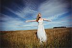 Woman standing with arms outstretched in wheat field on a sunny day