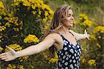 Woman standing with arms outstretched in meadow on a sunny day