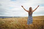 Rear view woman standing with arms outstretched in field