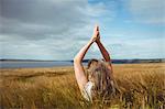 Woman with hands raised over head in prayer position in field on a sunny day