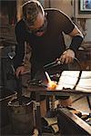 Glassblower working on a molten glass at glassblowing factory