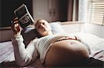 Pregnant woman looking at a sonography in bedroom at home