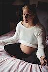Pregnant woman performing yoga in bedroom at home