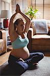Pregnant woman performing yoga in living room at home
