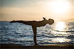 Woman performing yoga on beach on during sunset
